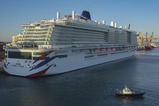 Massive gigantic modern cruiseship cruise ship liner Iona or Arvia in Cadiz, Spain during summer Mediterranean cruising with harbor and container port infrastructure