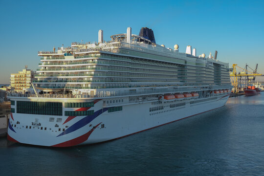 Massive gigantic modern cruiseship cruise ship liner Iona or Arvia in Cadiz, Spain during summer Mediterranean cruising with harbor and container port infrastructure