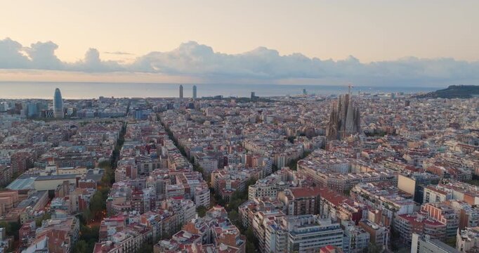 Cinematic aerial of Barcelona city skyline. Drone fly over Eixample residential famous urban grid and Sagrada Familia cathedral with morning sunrise cityscape. Catalonia, Spain. Travel Destination.