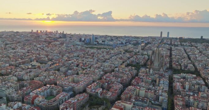 Cinematic aerial of Barcelona city skyline. Drone fly over Eixample residential famous urban grid and Sagrada Familia cathedral with morning sunrise cityscape. Catalonia, Spain. Travel Destination.
