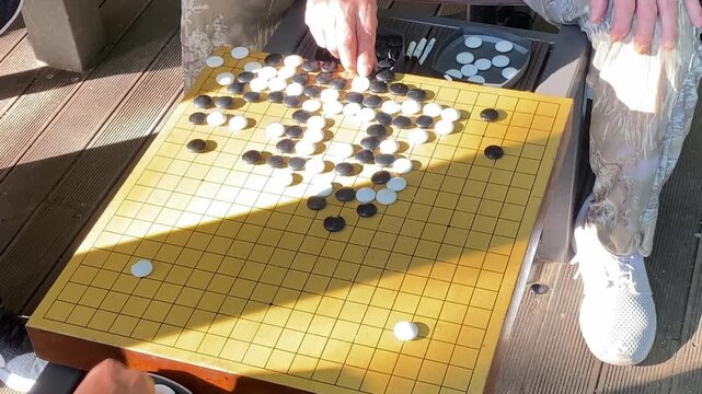 Close-up of senior hands placing a stone in a traditional Go board game outdoors