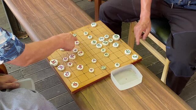 Close-up of senior hands playing a traditional Korean chess board game known as Janggi outdoors