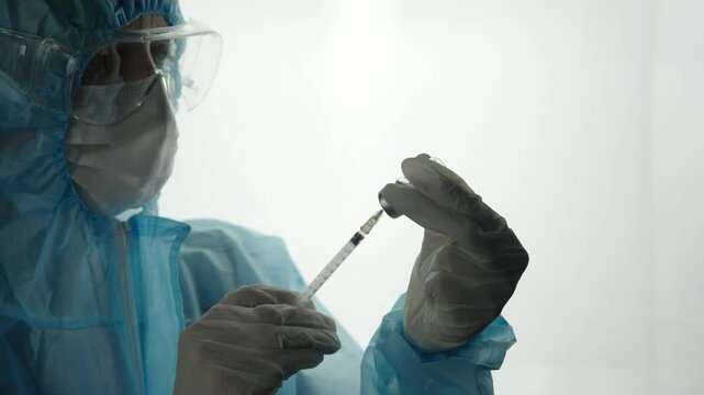 Doctor In Protective Suit Goggles Mask Filling Syringe From Vaccine Vial. Medical Research Laboratory Scientist