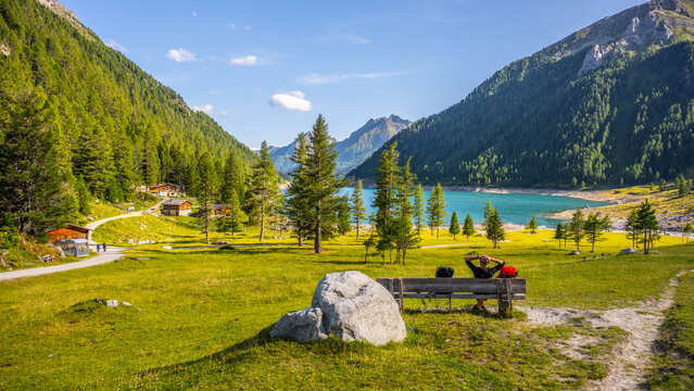 Visitors enjoy the view of Lake Neves in South Tyrol, located at the end of the Molini Valley in the Zillertal Alps, Italy. The area is surrounded by green trees and mountains.