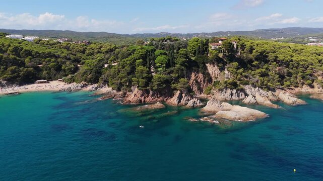 An aerial view of a drone flies over the beach, sea and coastal cliffs near Santa Clotilde Park on a sunny day in the tourist town of Lloret de Mar, Catalonia, Spain