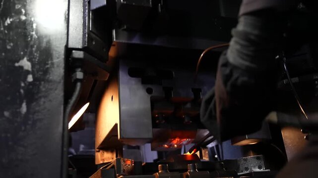 Worker adjusting a forging press machine with a glowing hot metal edge visible