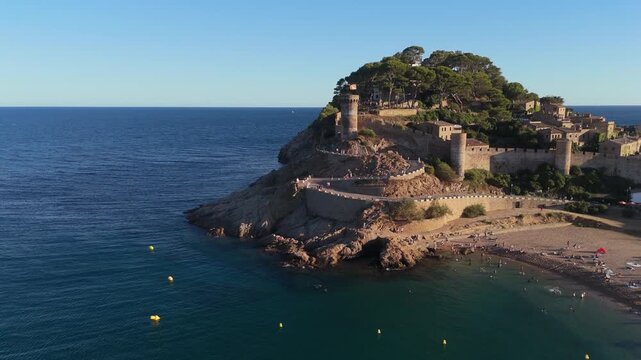 Aerial drone view of a fortress on coastal cliffs, a beach and the sea at sunset in the tourist town of Tossa de Mar, Catalonia, Spain