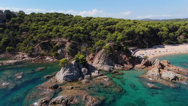 An aerial view of a drone flies over the beach, sea and coastal cliffs near Santa Clotilde Park on a sunny day in the tourist town of Lloret de Mar, Catalonia, Spain