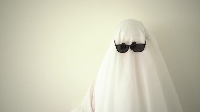 Minimal Halloween ghost cleaning dust from the shoulder, portrait looking to the side and white sheet costume,  with a mysterious and playful spooky appearance, copy space