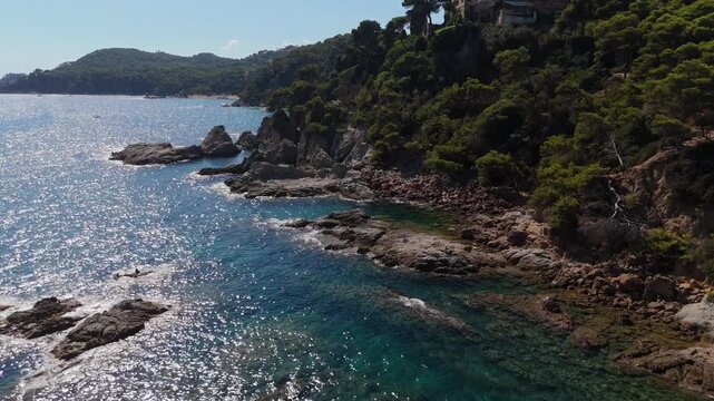 An aerial view of a drone flies over the beach, sea and coastal cliffs near Santa Clotilde Park on a sunny day in the tourist town of Lloret de Mar, Catalonia, Spain