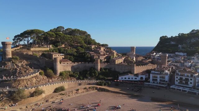 Aerial drone view of a fortress on coastal cliffs, a beach and the sea at sunset in the tourist town of Tossa de Mar, Catalonia, Spain