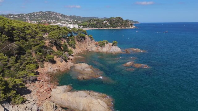 An aerial view of a drone flies over the beach, sea and coastal cliffs near Santa Clotilde Park on a sunny day in the tourist town of Lloret de Mar, Catalonia, Spain