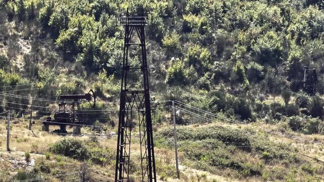 Industrial Oil Rig Metal Tower Derrick Standing Near Pumpjack In Forested Hillside Area. Fuel Energy Production Industry Infrastructure 