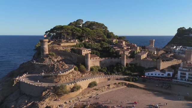 Aerial drone view of a fortress on coastal cliffs, a beach and the sea at sunset in the tourist town of Tossa de Mar, Catalonia, Spain