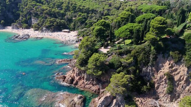 An aerial view of a drone flies over the beach, sea and coastal cliffs near Santa Clotilde Park on a sunny day in the tourist town of Lloret de Mar, Catalonia, Spain
