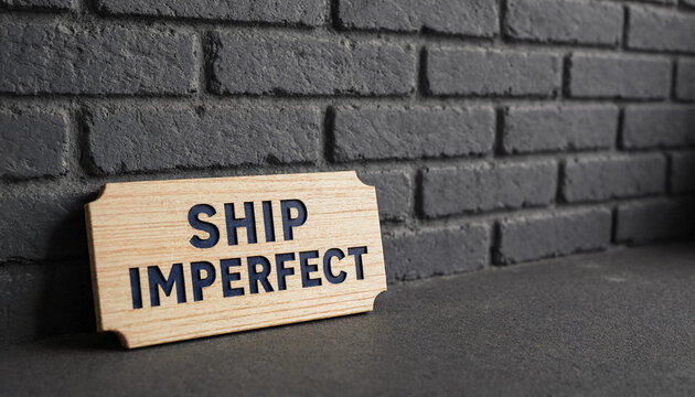 Wooden sign with ship imperfect text leaning against dark brick wall concept for business iteration and progress