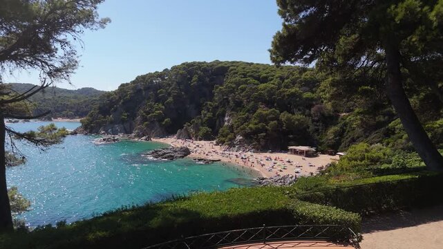 An aerial view of a drone flies from Santa Clotilde Park over the beach and coastal cliffs on a sunny day in the tourist town of Lloret De Mar, Catalonia, Spain.