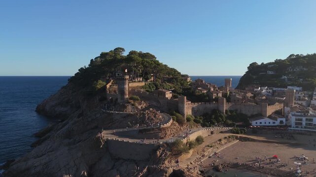 Aerial drone view of a fortress on coastal cliffs, a beach and the sea at sunset in the tourist town of Tossa de Mar, Catalonia, Spain