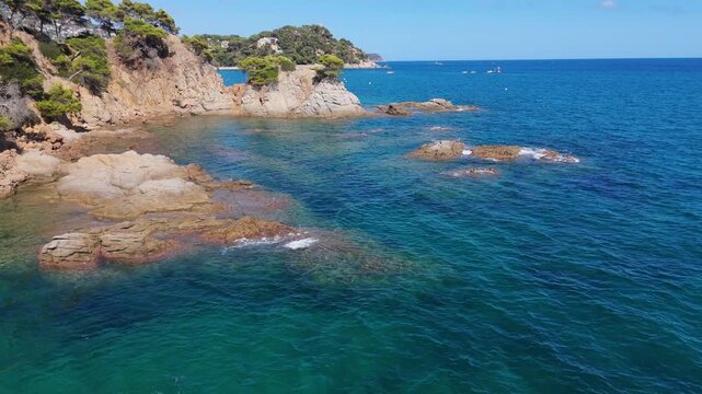 An aerial view of a drone flies over the beach, sea and coastal cliffs near Santa Clotilde Park on a sunny day in the tourist town of Lloret de Mar, Catalonia, Spain