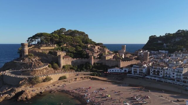 Aerial drone view of a fortress on coastal cliffs, a beach and the sea at sunset in the tourist town of Tossa de Mar, Catalonia, Spain
