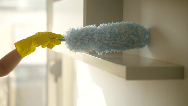Woman In Yellow Rubber Glove Dusting Shelf Surface With Microfiber Duster Brush. Housekeeping Furniture Dust Cleaning 