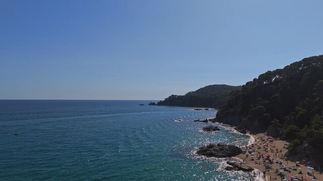 An aerial view of a drone flies from Santa Clotilde Park over the beach and coastal cliffs on a sunny day in the tourist town of Lloret De Mar, Catalonia, Spain.
