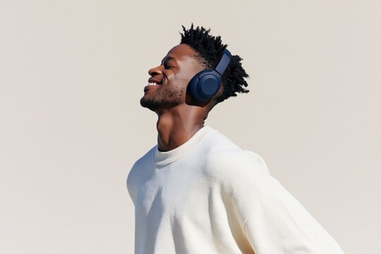 Joyful young man wearing dark headphones looking upward with neutral backdrop for wallpaper or banner design and lifestyle use