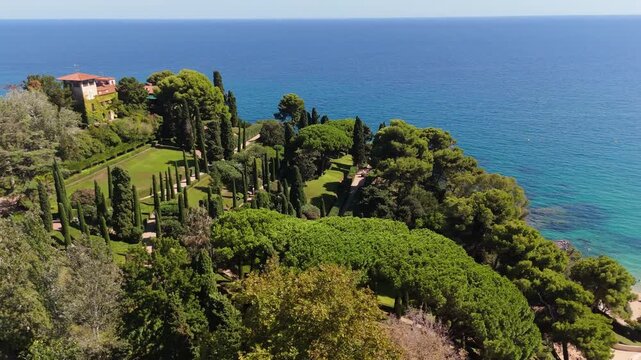 An aerial view of a drone flies from Santa Clotilde Park over the beach and coastal cliffs on a sunny day in the tourist town of Lloret De Mar, Catalonia, Spain.