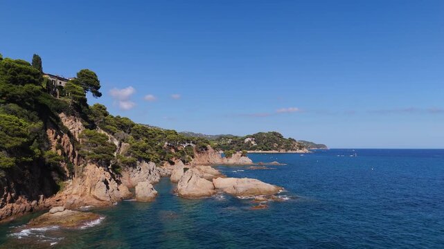An aerial view of a drone flies over the beach, sea and coastal cliffs near Santa Clotilde Park on a sunny day in the tourist town of Lloret de Mar, Catalonia, Spain