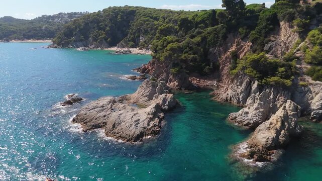 An aerial view of a drone flies over the beach, sea and coastal cliffs near Santa Clotilde Park on a sunny day in the tourist town of Lloret de Mar, Catalonia, Spain