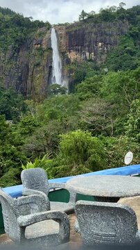 Young woman walking towards table to enjoy scenic view of Diyaluma waterfall in Sri Lanka.