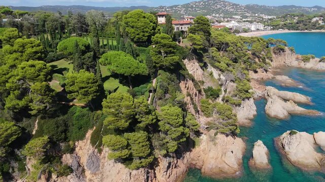 An aerial view of a drone flies over the beach, sea and coastal cliffs near Santa Clotilde Park on a sunny day in the tourist town of Lloret de Mar, Catalonia, Spain