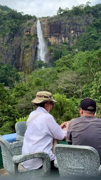 Couple sitting at cafe table enjoying scenic view of Diyaluma waterfall in Sri Lanka.