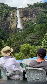 Couple sitting at cafe table enjoying scenic view of Diyaluma waterfall in Sri Lanka.