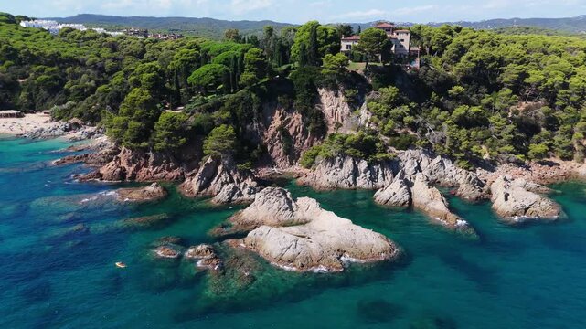 An aerial view of a drone flies over the beach, sea and coastal cliffs near Santa Clotilde Park on a sunny day in the tourist town of Lloret de Mar, Catalonia, Spain