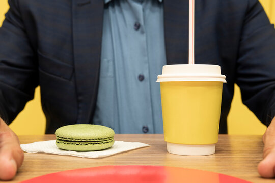 businessman has breakfast in a cafe, drinks coffee and eats a sweet French cake. Breakfast concept in a street cafe. Coffee with macaroons on a wooden background.