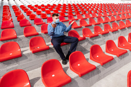 lonely man with a protective mask on his face is sitting and watching a sports competition alone on a large empty grandstand. Competition and other mass events during the lockdown.