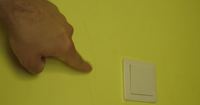 Close-up of a man pointing at a visible crack in an interior wall, representing structural damage, building defects, home inspection and necessary repair.