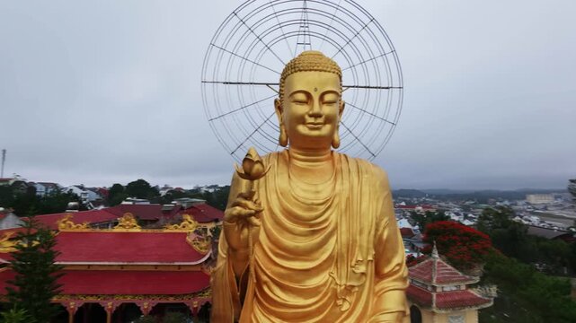 Panning shot of large golden buddha overlooking city skyline on cloudy day