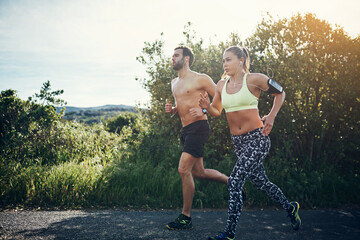 Obraz premium Fitness, couple or running with earphones on road for outdoor workout or cardio exercise together. Active, man and woman with sunshine or music for mountain challenge, health or wellness in nature