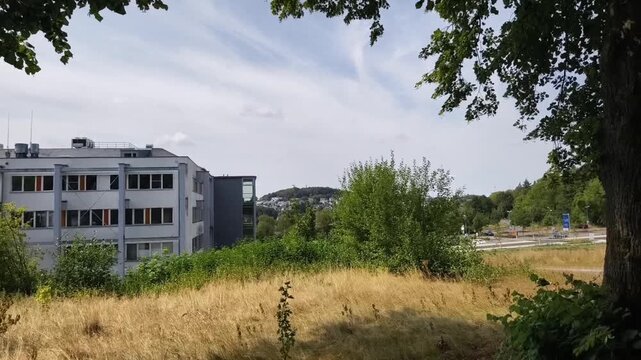 Zeitlupen Schwenk vom Krankenhaus zur Tagesklinik in Brilon, Deutschland. Umgeben von Natur und B&auml;umen liegen die Geb&auml;ude im Gr&uuml;nen.