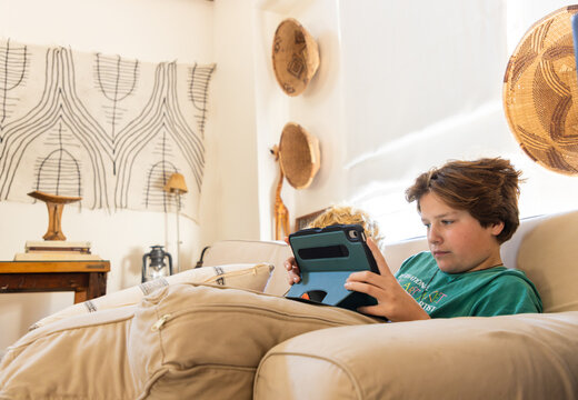 teenage boy playing video game on tablet relaxing on couch at home