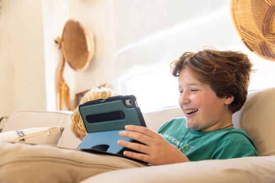 teenage boy playing video game on tablet relaxing on couch at home