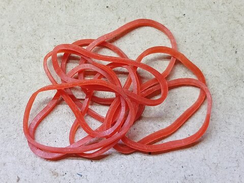 Red Rubber Band Twisted Into Loops On A Gray Concrete Surface