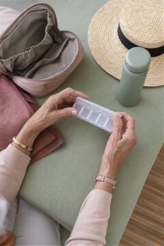Senior woman holding empty pill organizer while preparing for travel. Elderly female packing vitamins and medication into handbag for vacation.