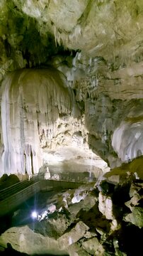 Vast interior of the New Athos Cave in Abkhazia featuring dramatic stalactite and flowstone formations illuminated by artificial lights, with tourist walkways navigating the underground landscape