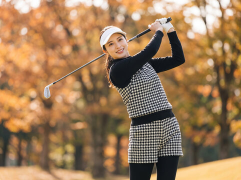 紅葉したゴルフ場でスイングを終え笑顔を見せる女性