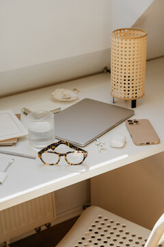 Cozy Attic Home Office Still Life With Glasses, Closed Laptop, And Rattan Lamp Under Sunlight