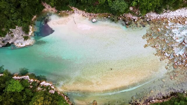 Overhead aerial drone view of a wide clear pool with a pale gravel bottom at a bend of the emerald river, Soca Valley, Slovenia