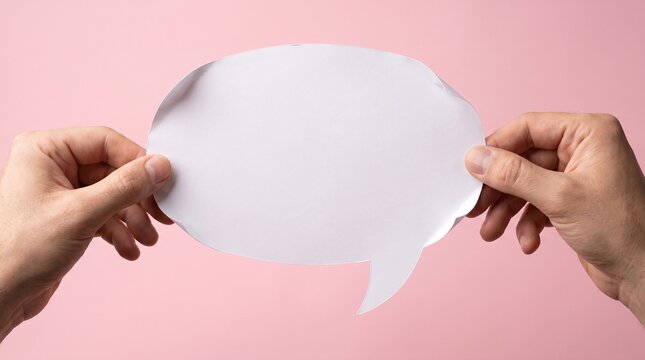Two hands holding a blank white speech bubble cutout against a soft pink background